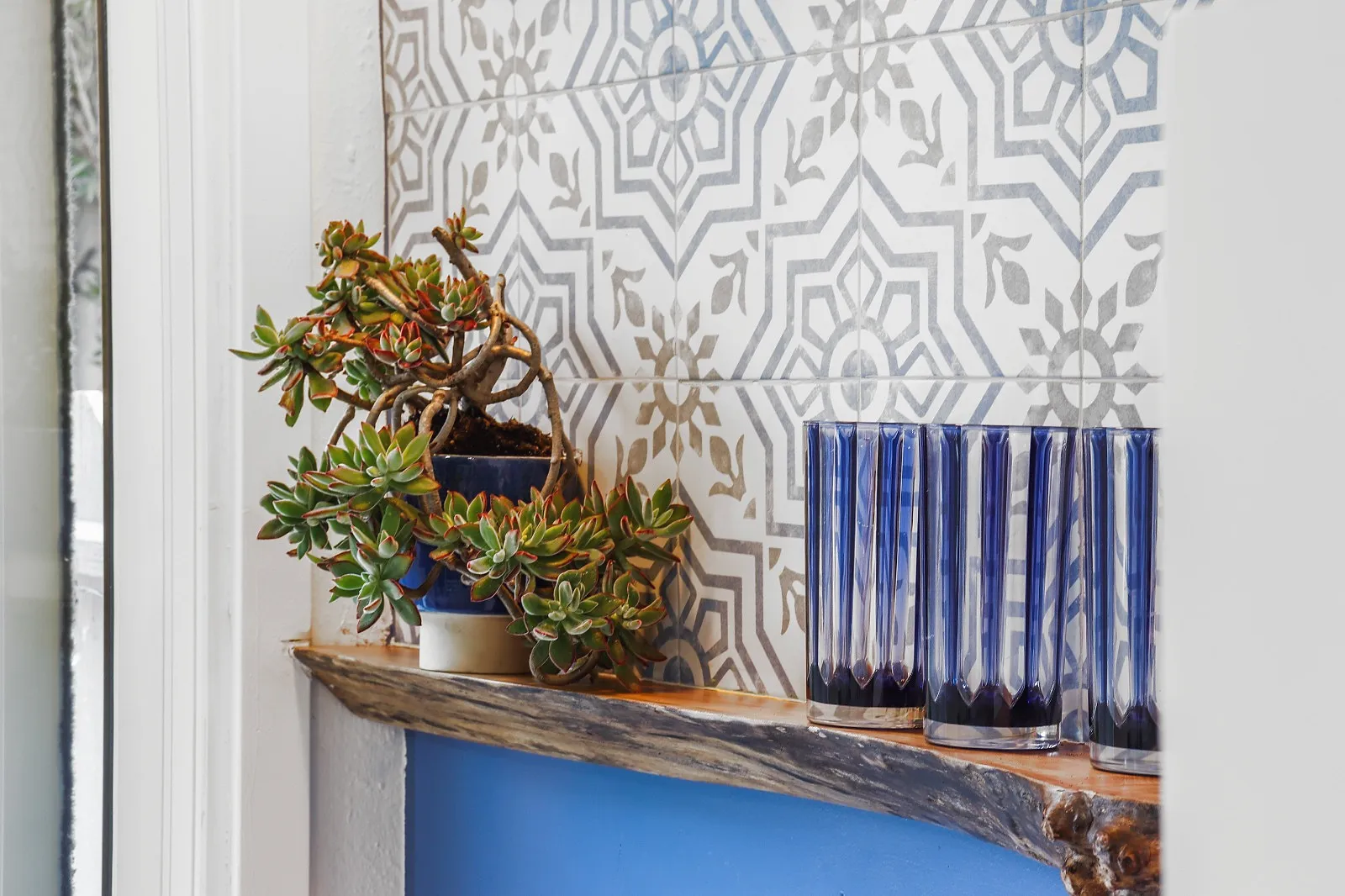 Kitchen feature wall in patterned tile with open timber shelving and potted plants