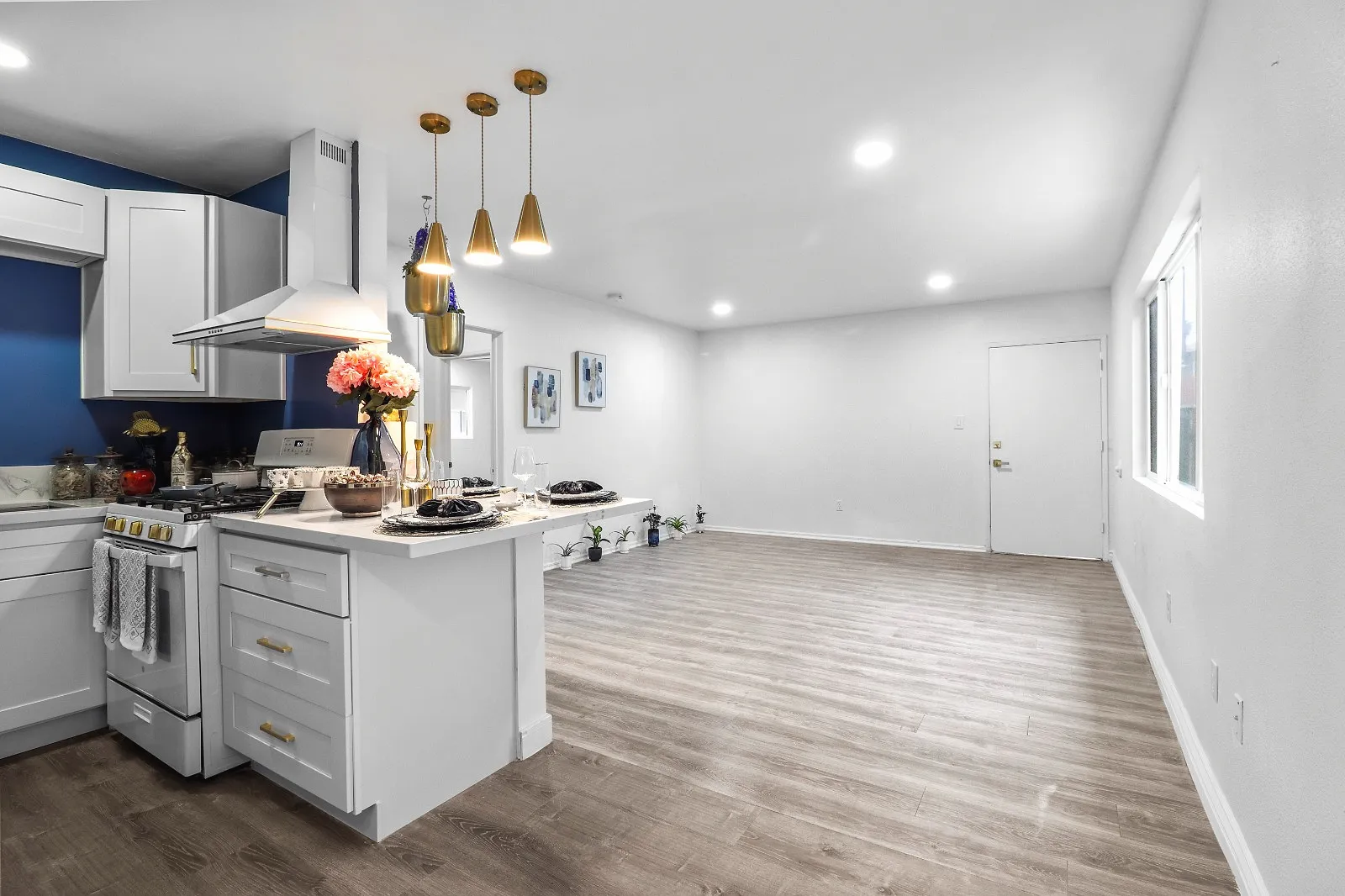 Finished open-plan kitchen with white shaker cabinets, a quartz peninsula, brass pendant lights, a deep blue accent wall and wood-look flooring