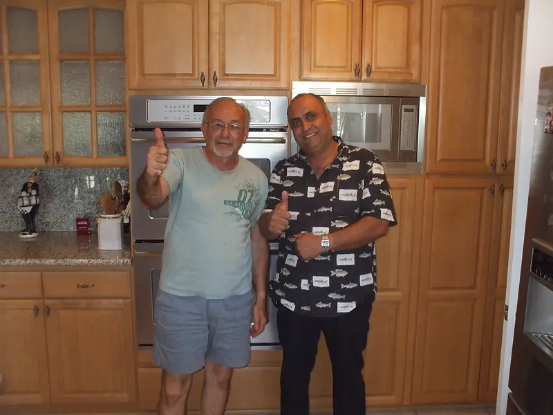 Two men giving a thumbs-up in a completed kitchen, in front of maple cabinets and a stainless built-in oven