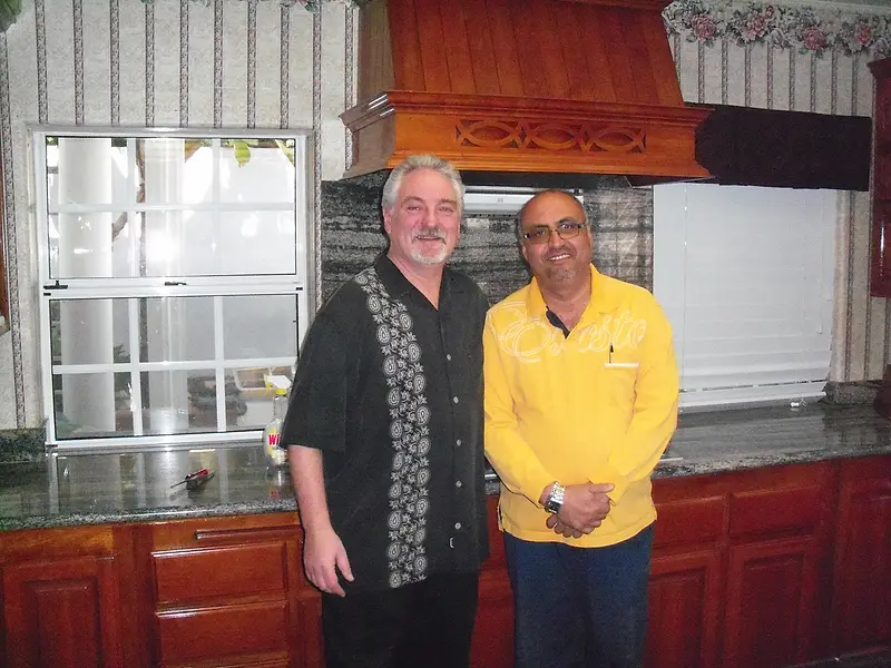 Two men standing in a finished kitchen with cherry cabinetry, granite worktops and a carved timber range hood